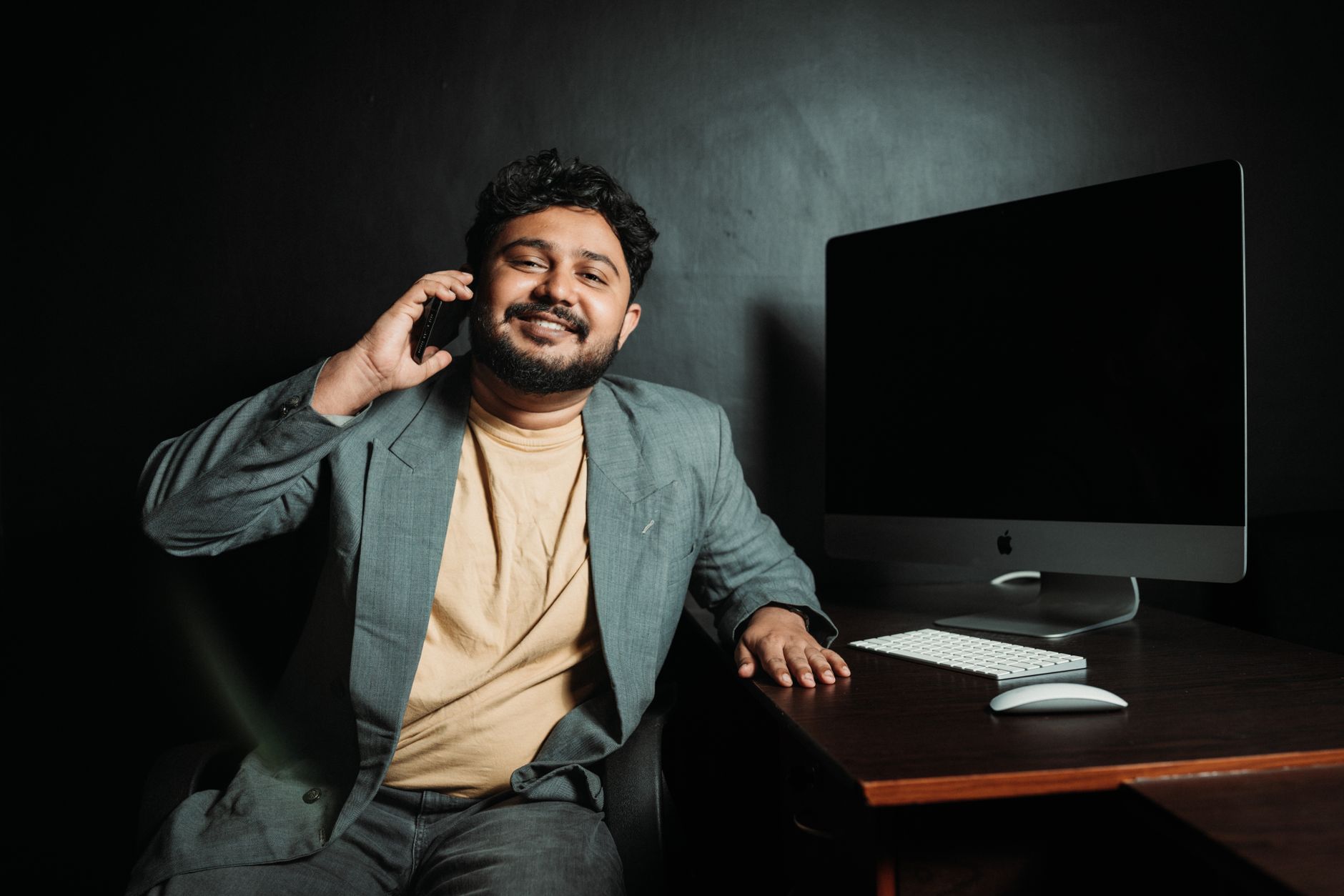 Smiling businessman in a suit talking on the phone at a desk with a computer.