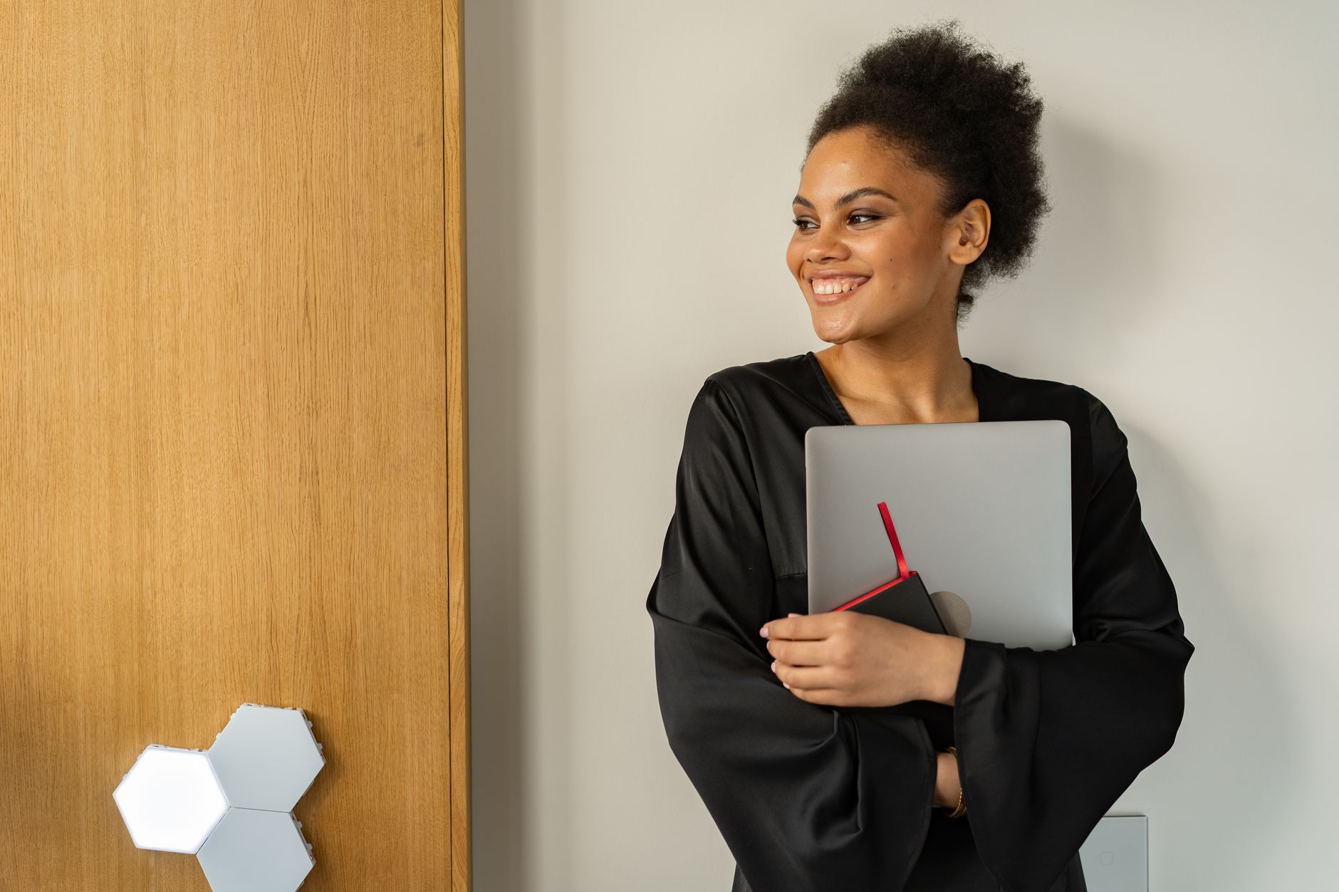Smiling woman with afro holding a laptop indoors, exuding confidence and positivity.